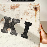 a close-up view of a white canvas with a large, bold black letter "K" prominently displayed. The canvas appears to be in a somewhat worn and aged condition, with visible rust and scratches.