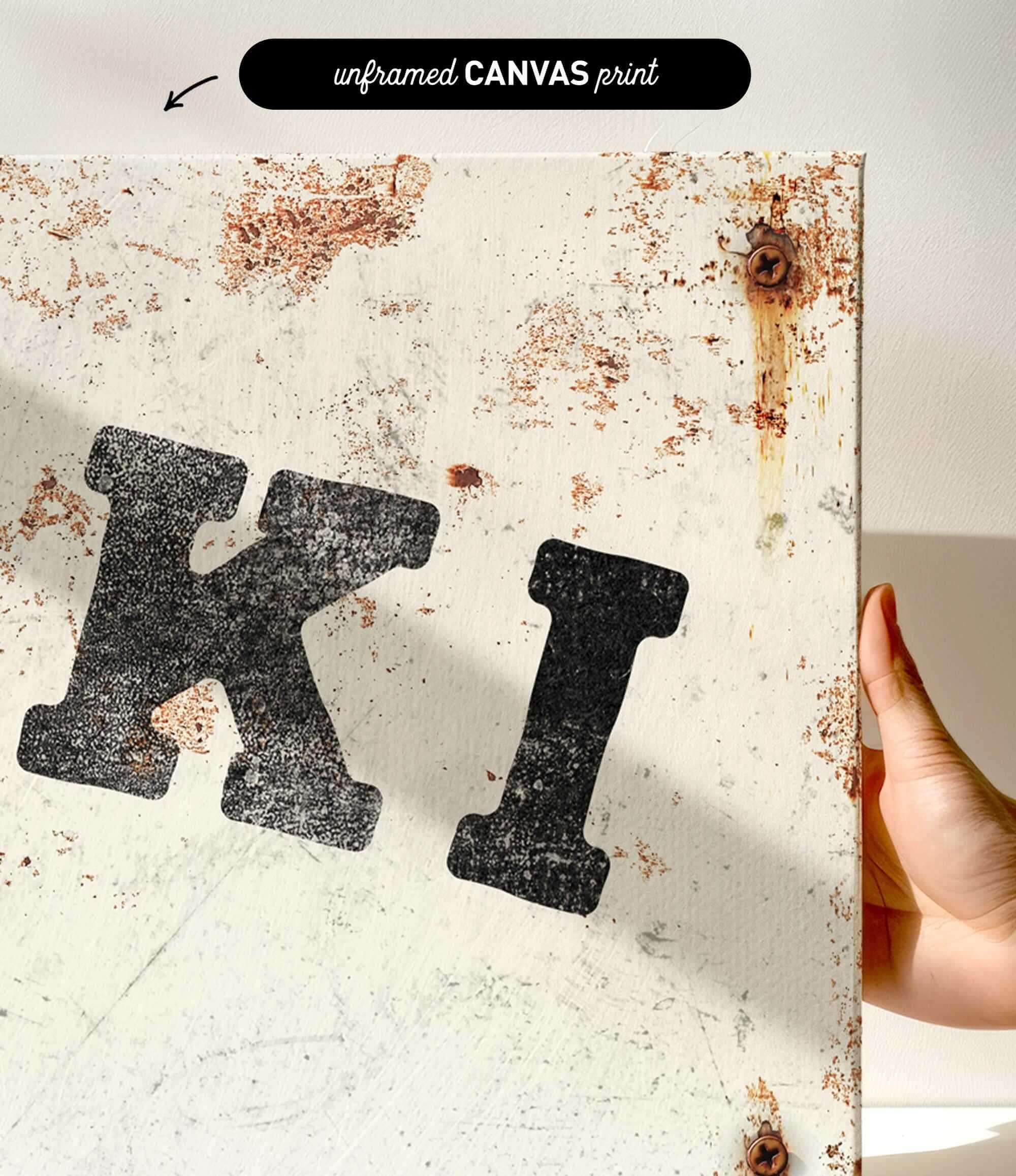 a close-up view of a white canvas with a large, bold black letter "K" prominently displayed. The canvas appears to be in a somewhat worn and aged condition, with visible rust and scratches.