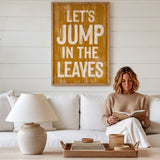 A woman is sitting on a white couch, reading a book, with a wooden sign above her that says "Let's JUMP in the LEAVES".