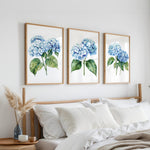 a bedroom with a bed, white pillows, and a framed artwork of blue hydrangeas hanging on the wall above it.