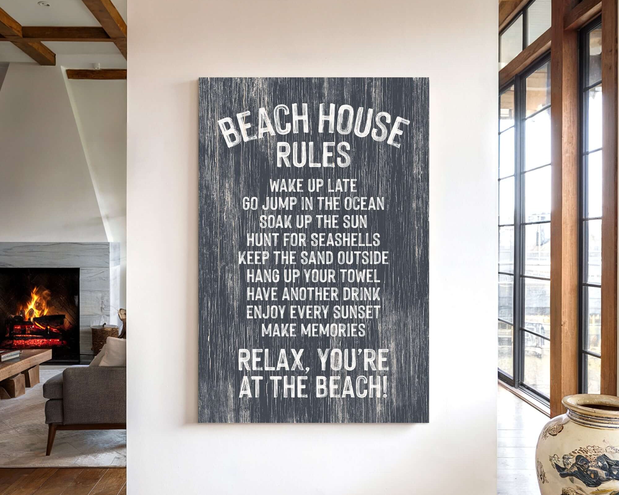 a sign on a wall that reads "BEACH HOUSE RULES" and provides a list of beach-related activities and behaviors, such as "WAKE UP LATE", "JUMP IN THE OCEAN", "SOAK UP THE SUN", "HUNT FOR SEAShells", "KEEP THE SAND OUTSIDE", "HANG UP YOUR TOWEL", "HAVEN DRINK", "ENJOY EVERY SUNSET", "MAKE MEMORIES", and "RELAX. YOU'RE AT THE BEACH!".