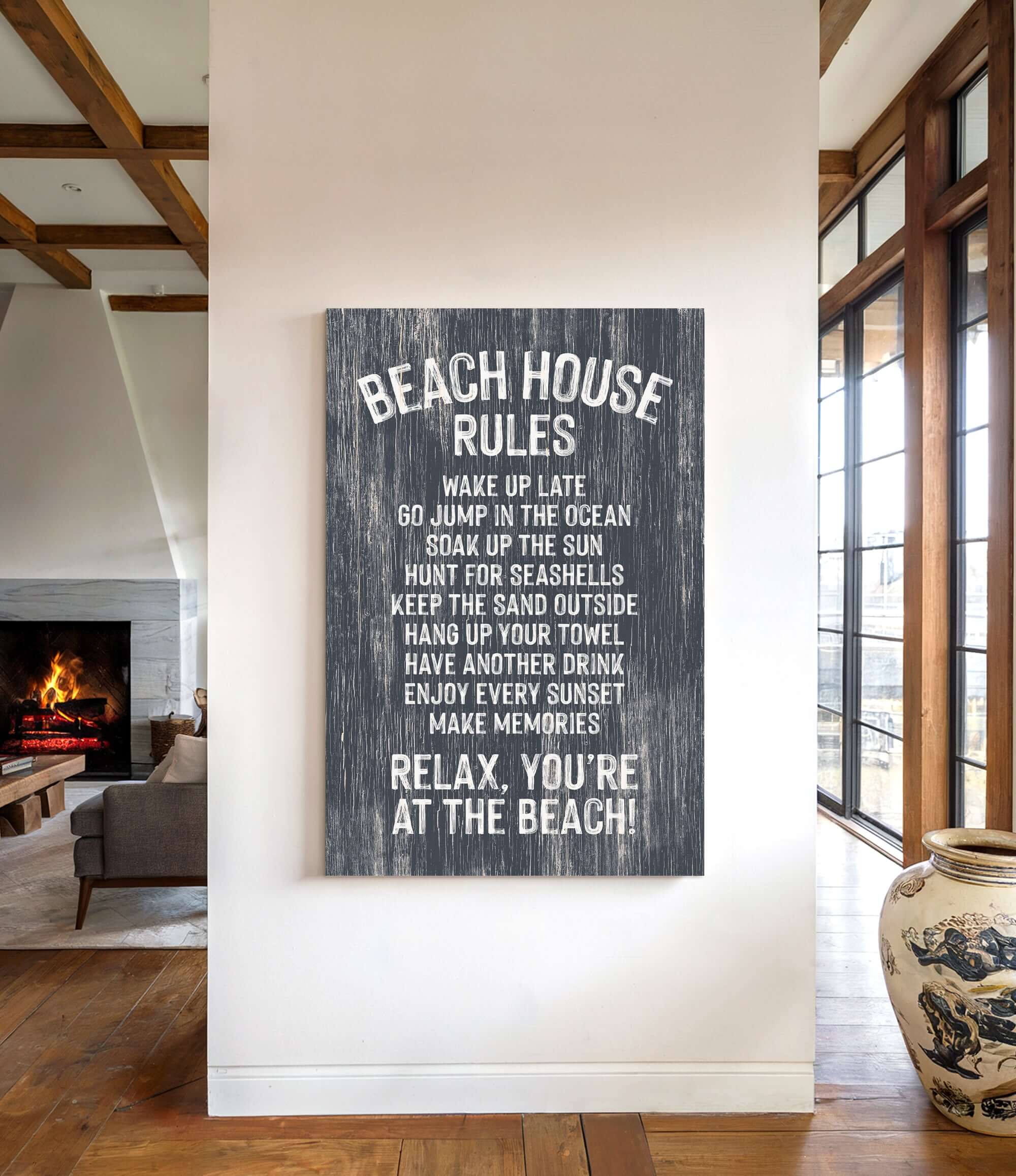 a sign on a wall that reads "BEACH HOUSE RULES" and provides a list of beach-related activities and behaviors, such as "WAKE UP LATE", "JUMP IN THE OCEAN", "SOAK UP THE SUN", "HUNT FOR SEAShells", "KEEP THE SAND OUTSIDE", "HANG UP YOUR TOWEL", "HAVEN DRINK", "ENJOY EVERY SUNSET", "MAKE MEMORIES", and "RELAX. YOU'RE AT THE BEACH!".