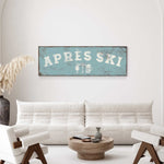 a living room with a white sofa, a wooden coffee table, and a decorative vase. Above the sofa, there is a vintage-style sign that says "APRES SKI" with a beer mug and a wine glass icon.