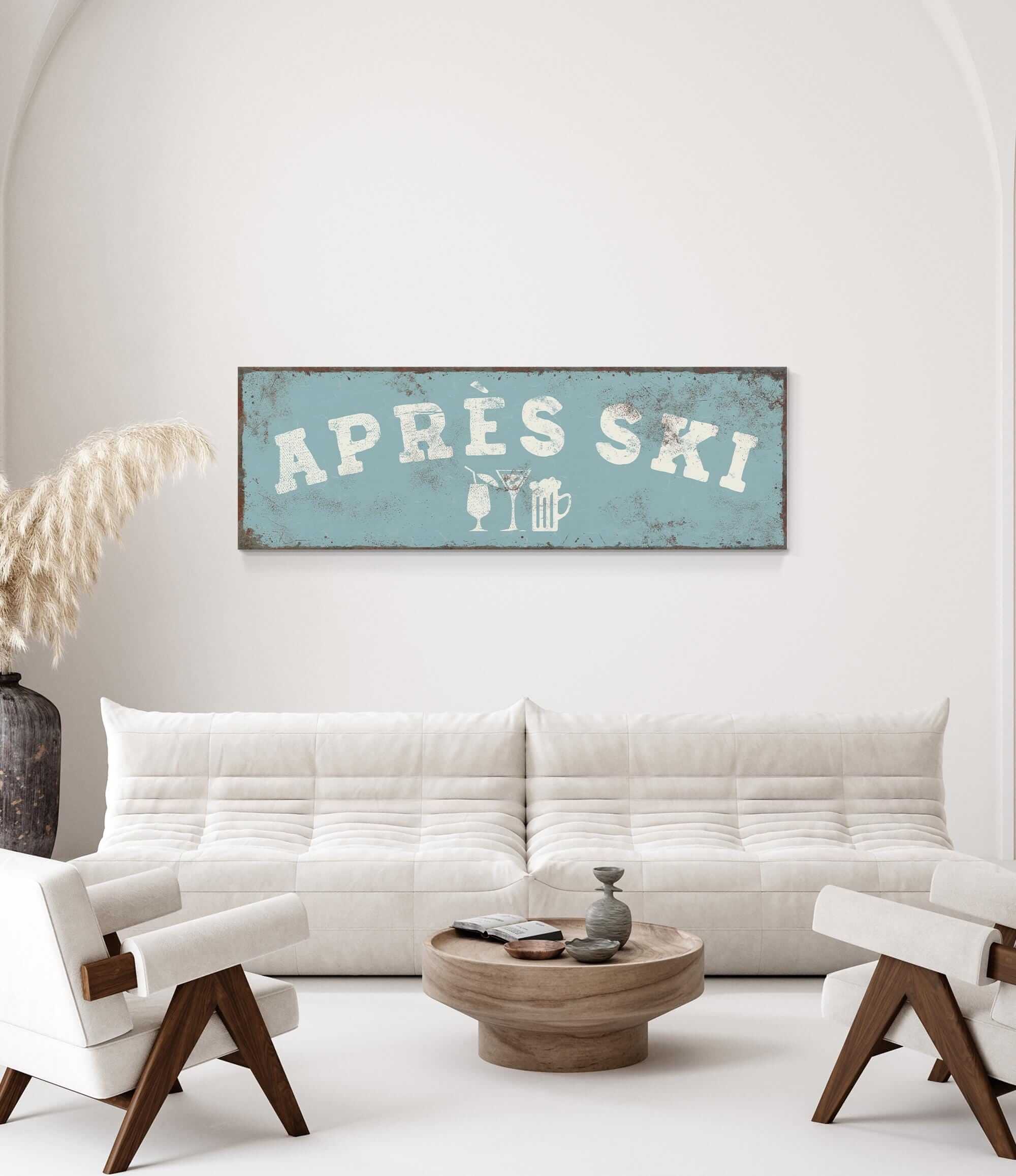 a living room with a white sofa, a wooden coffee table, and a decorative vase. Above the sofa, there is a vintage-style sign that says "APRES SKI" with a beer mug and a wine glass icon.