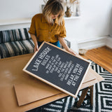 A woman in a yellow shirt is holding a black sign with white text, which appears to be a message or notice.