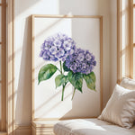 a large framed painting of purple hydrangeas on a white wall, with a wooden frame. The painting is placed in a corner of a room with a white couch and a window, creating a cozy and inviting atmosphere.