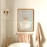A framed poster with a cartoon image of a dog sitting in a bathtub, along with the text "WASH YOUR PAWS" is displayed on the wall above a white bathtub in a bathroom.