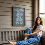 A woman is sitting on a bench in front of a sign that provides rules for the Lake House.