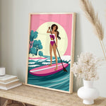 A framed illustration of a woman paddleboarding on a pink surfboard, with a pink and green background depicting a beach scene.