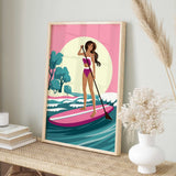 A framed illustration of a woman paddleboarding on a pink surfboard, with a pink and green background depicting a beach scene.