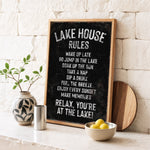 A blackboard sign with white text, a wooden board, a vase with a plant, a bowl of lemons, and a metal container on a white countertop.