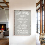 a sign that reads "LAKESHOUSE RULES" hanging on a wall in a room with a fireplace and a large window.