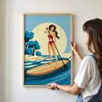 A woman is standing on a surfboard and holding a paddle, with a beach scene in the background.