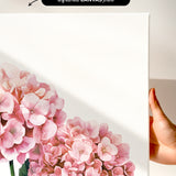 a hand holding a white canvas print of a floral design, with a focus on pink hydrangea flowers.
