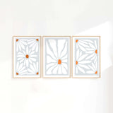 three white and orange art pieces hanging on a wall