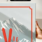 a hand holding a framed print of a mountain landscape with skis and ski poles.