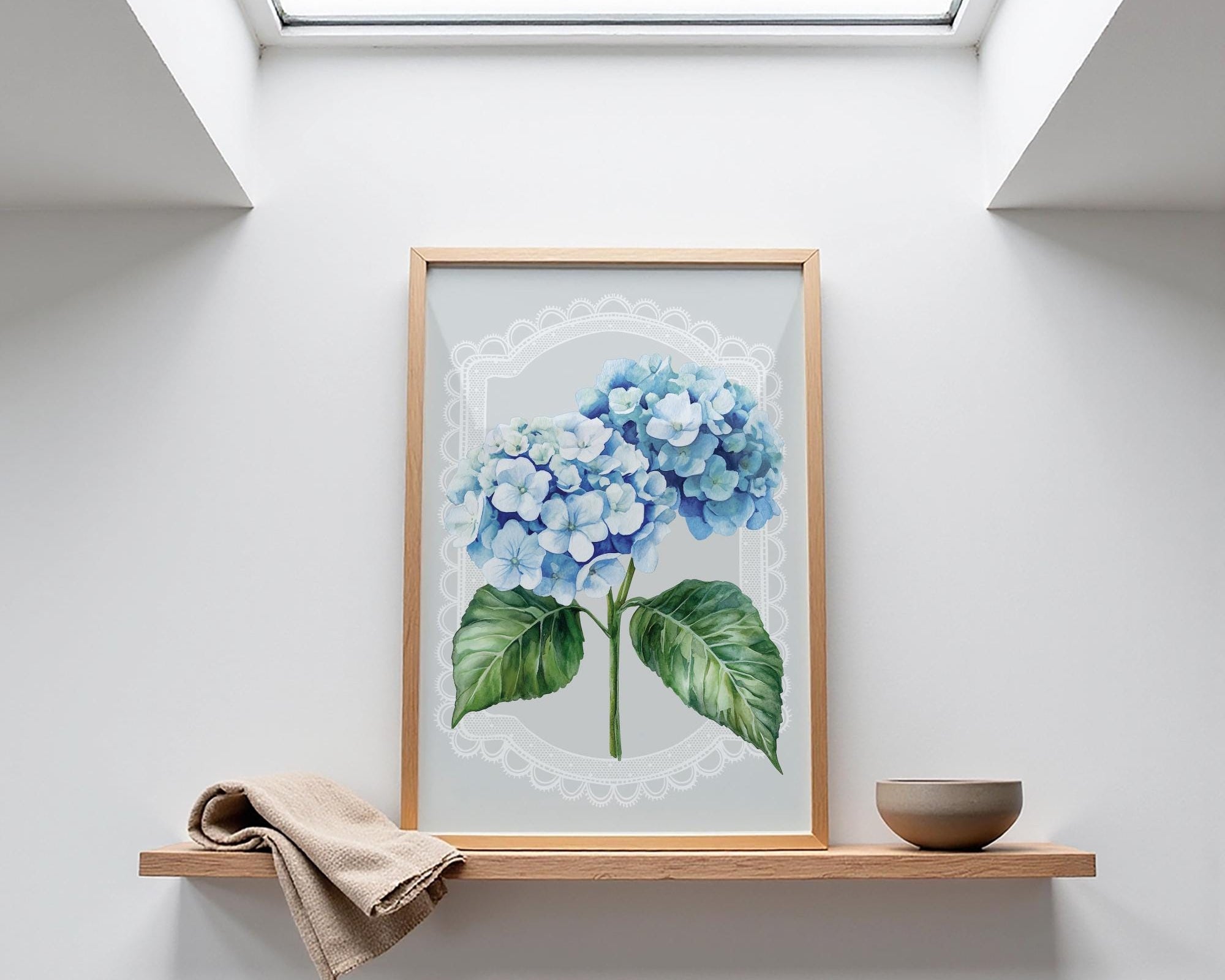 a framed painting of blue hydrangeas on a shelf, with a small bowl and a towel placed next to it.