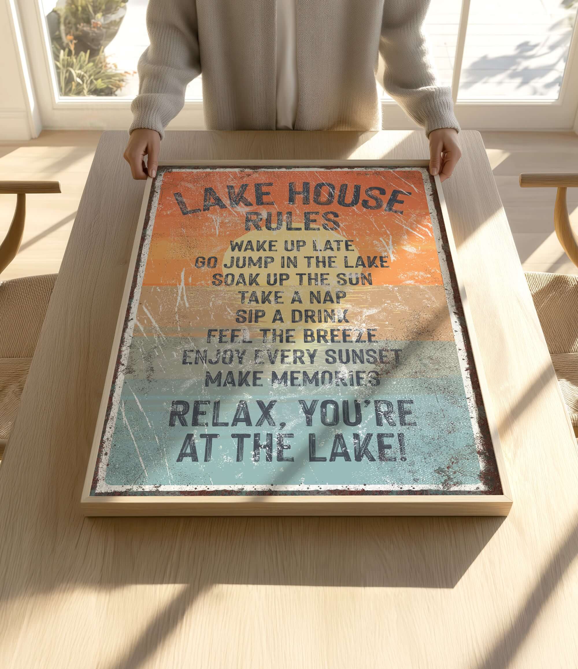 A person is holding up a framed sign with a list of rules for a lake house, including activities such as waking up late, jumping in the lake, taking a nap, and enjoying the sunset.