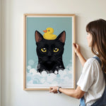 A woman is hanging a framed picture of a black cat with a yellow rubber duck on its head.