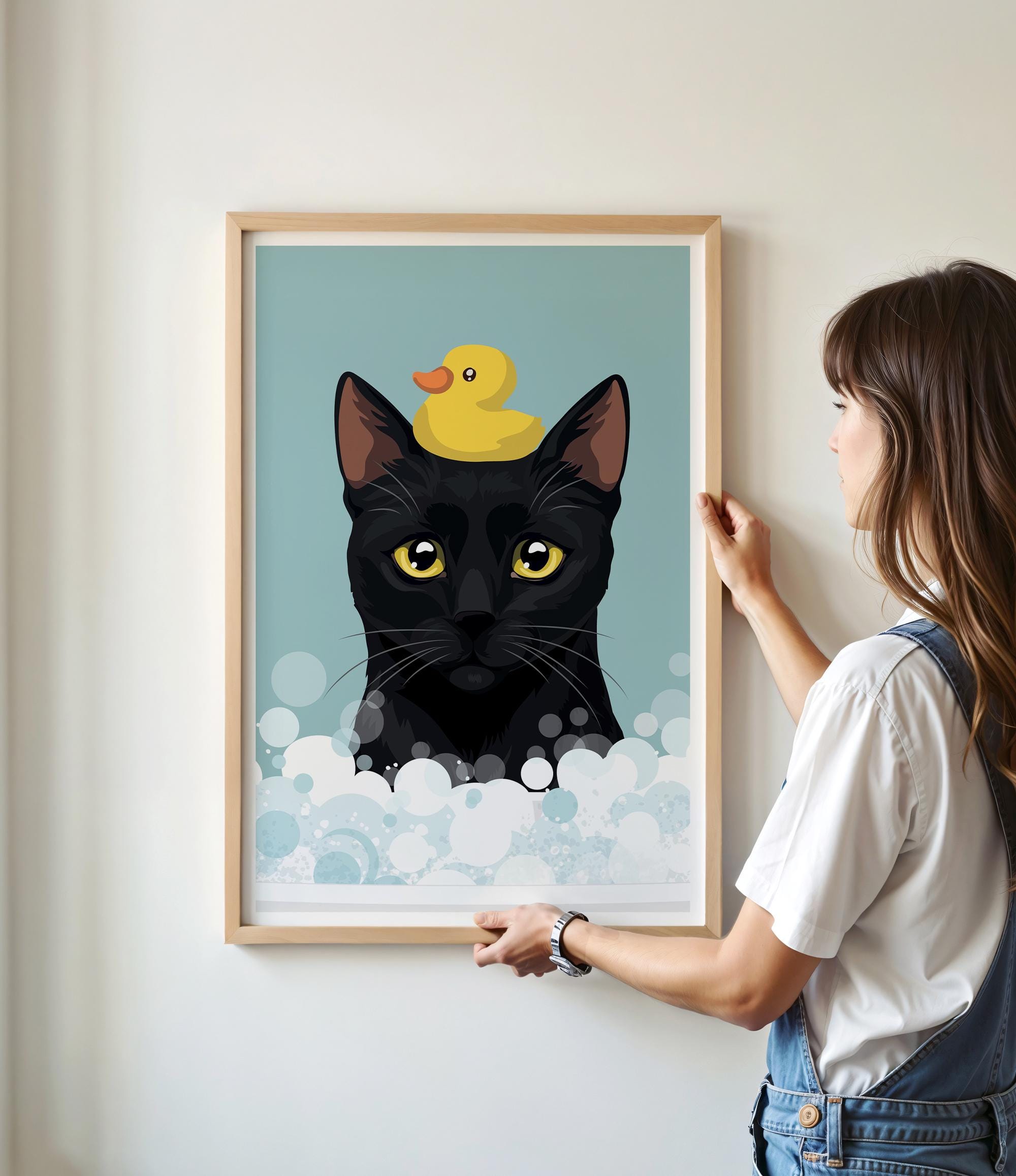 A woman is hanging a framed picture of a black cat with a yellow rubber duck on its head.