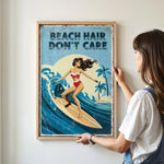 A woman is hanging a framed poster on a wall that features an illustration of a woman surfing on a wave.