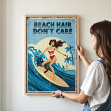 A woman is hanging a framed poster on a wall that features an illustration of a woman surfing on a wave.