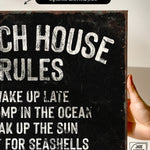 a hand holding a sign that says beach house rules