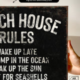 a hand holding a sign that says beach house rules