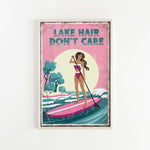 A framed poster with a woman paddleboarding on a lake, with the text "LAKESHAIR DON'T CARE" written above her.