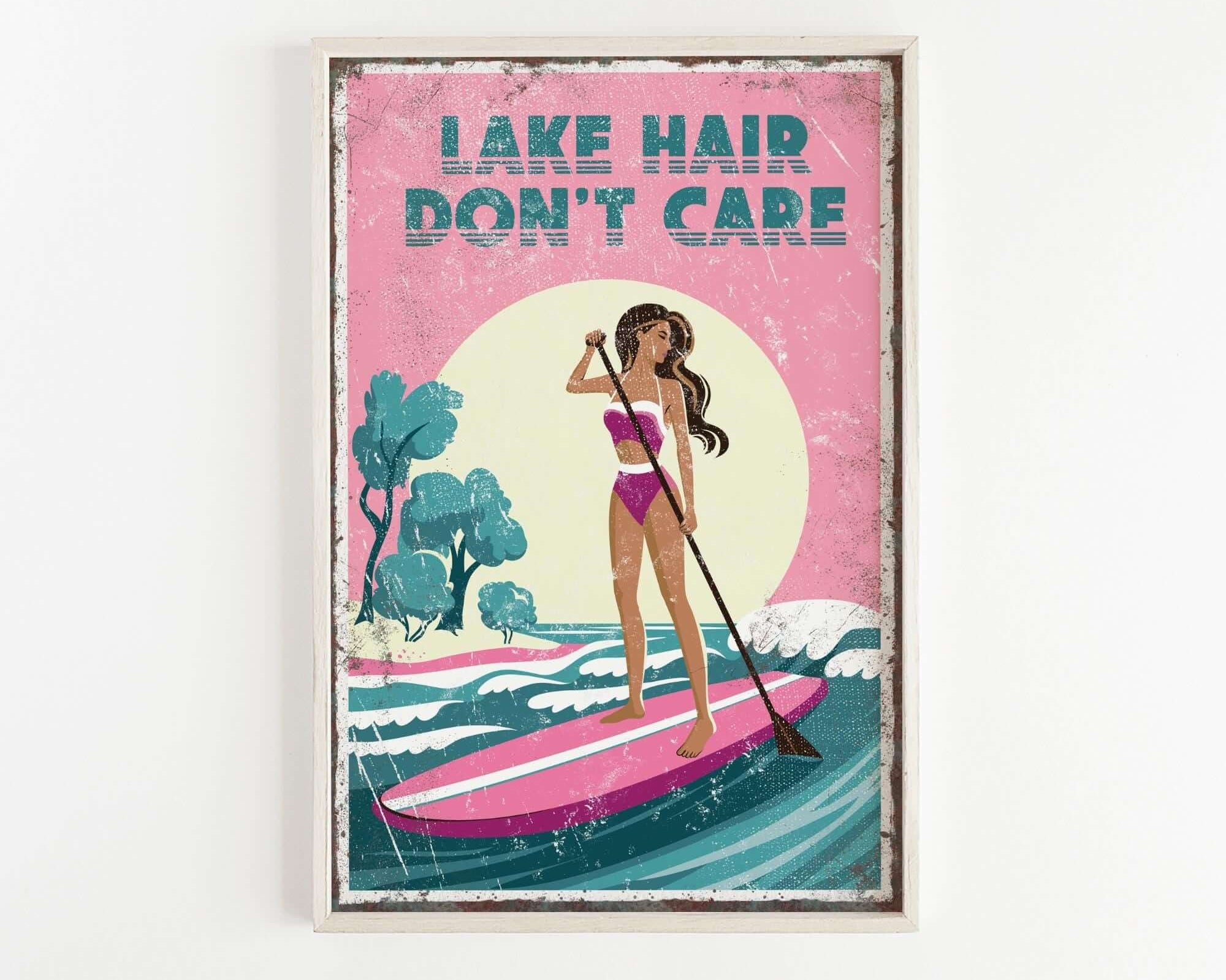 A framed poster with a woman paddleboarding on a lake, with the text "LAKESHAIR DON'T CARE" written above her.