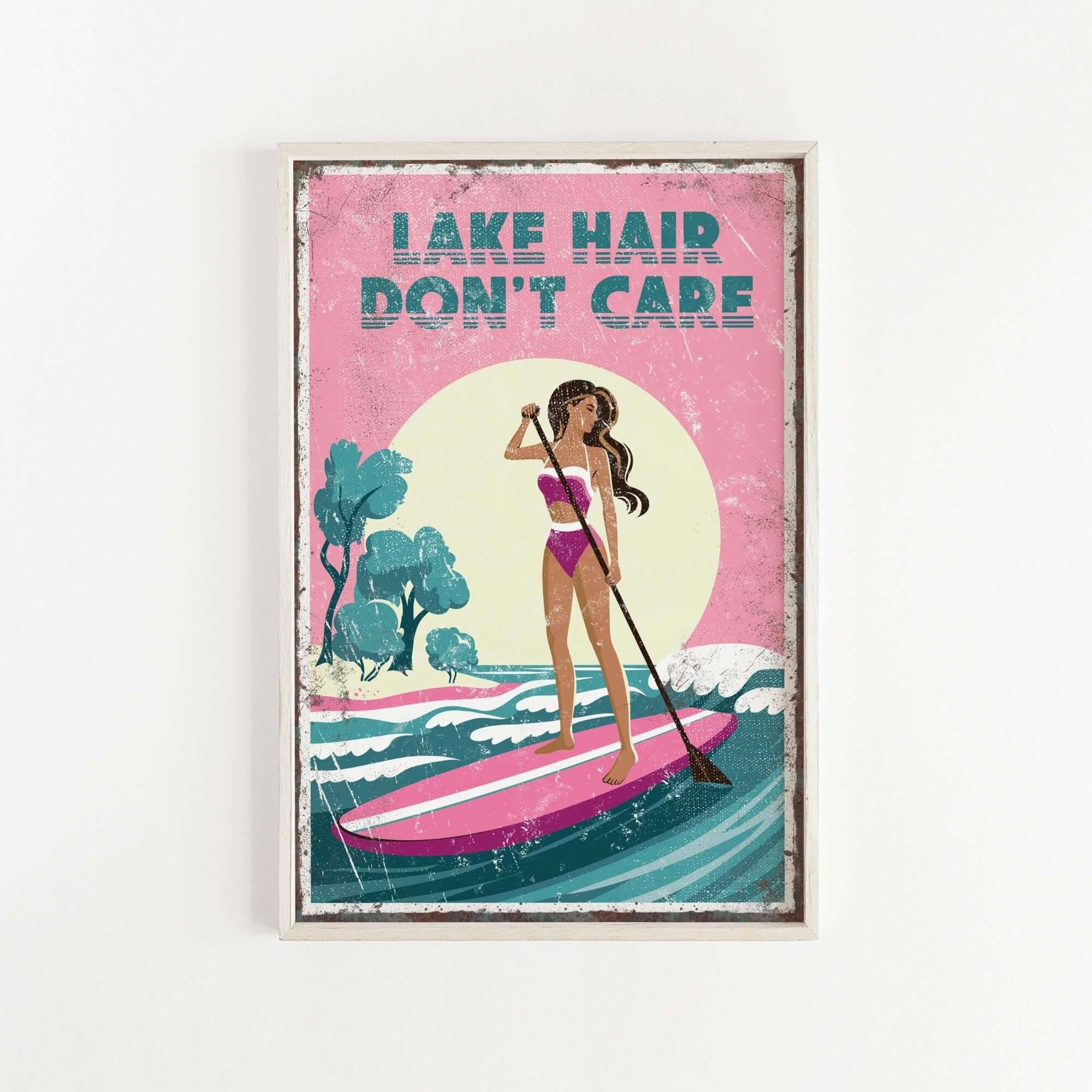 A framed poster with a woman paddleboarding on a lake, with the text "LAKESHAIR DON'T CARE" written above her.