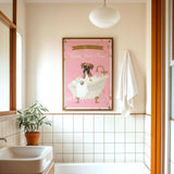 a bathroom with a pink bathtub, a towel, a plant, and a framed poster of a dog in a bathtub.