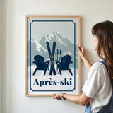 A woman is standing in front of a framed poster that features a mountain landscape with two Adirondack chairs and skis, along with the text "Apres-ski".
