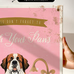 a hand holding a framed print with a dog's face and the text "Don't forget to wash your paws" on it.