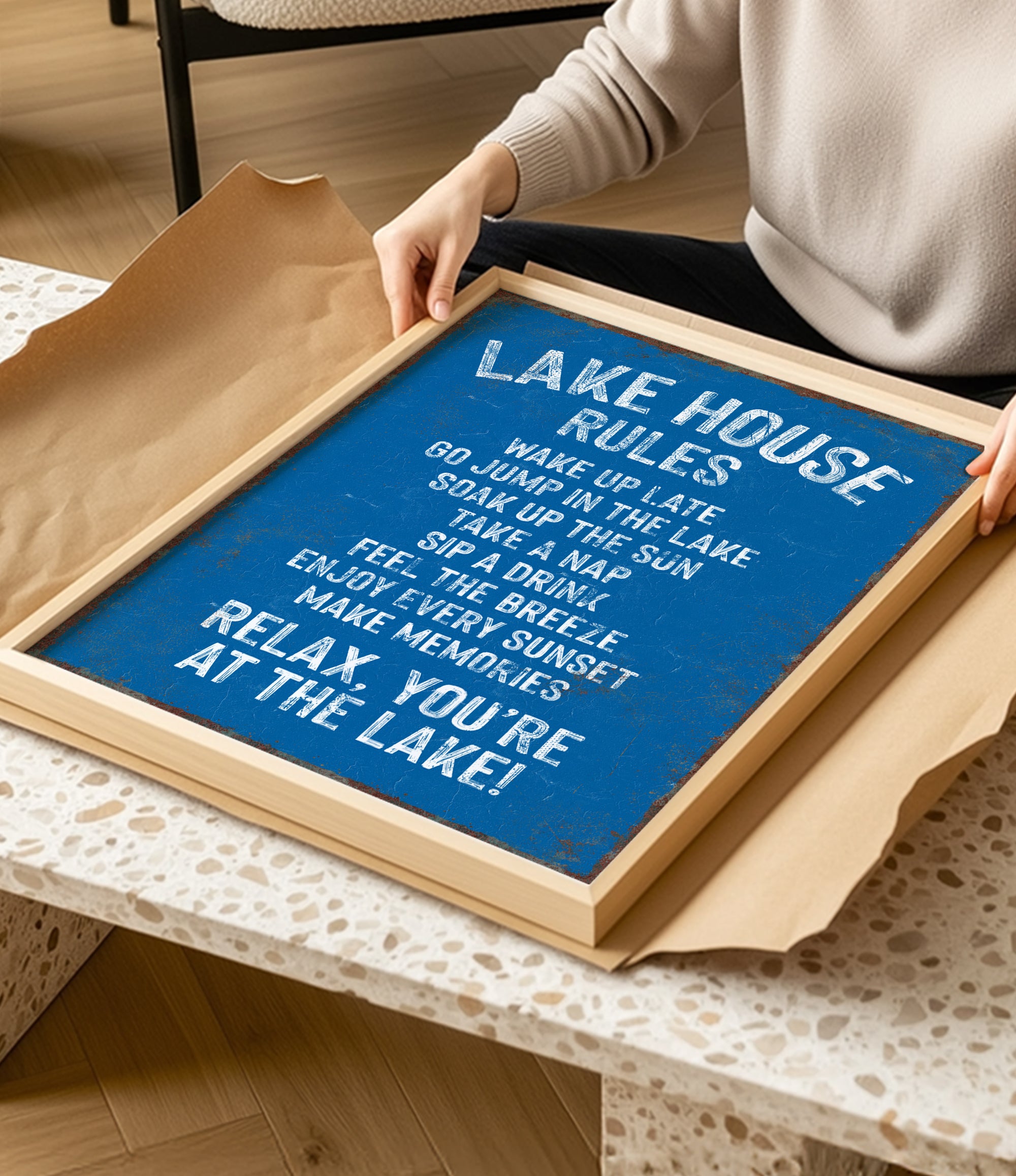 A person is holding a framed sign with a blue background and white text, which appears to be a list of rules or instructions for a lake house.