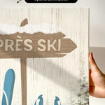 A hand holds the Cerulean Après Ski Signpost Wall Art, a rustic vintage ski sign canvas with blue ski gear—ideal mountain lodge decor for après ski artwork enthusiasts.
