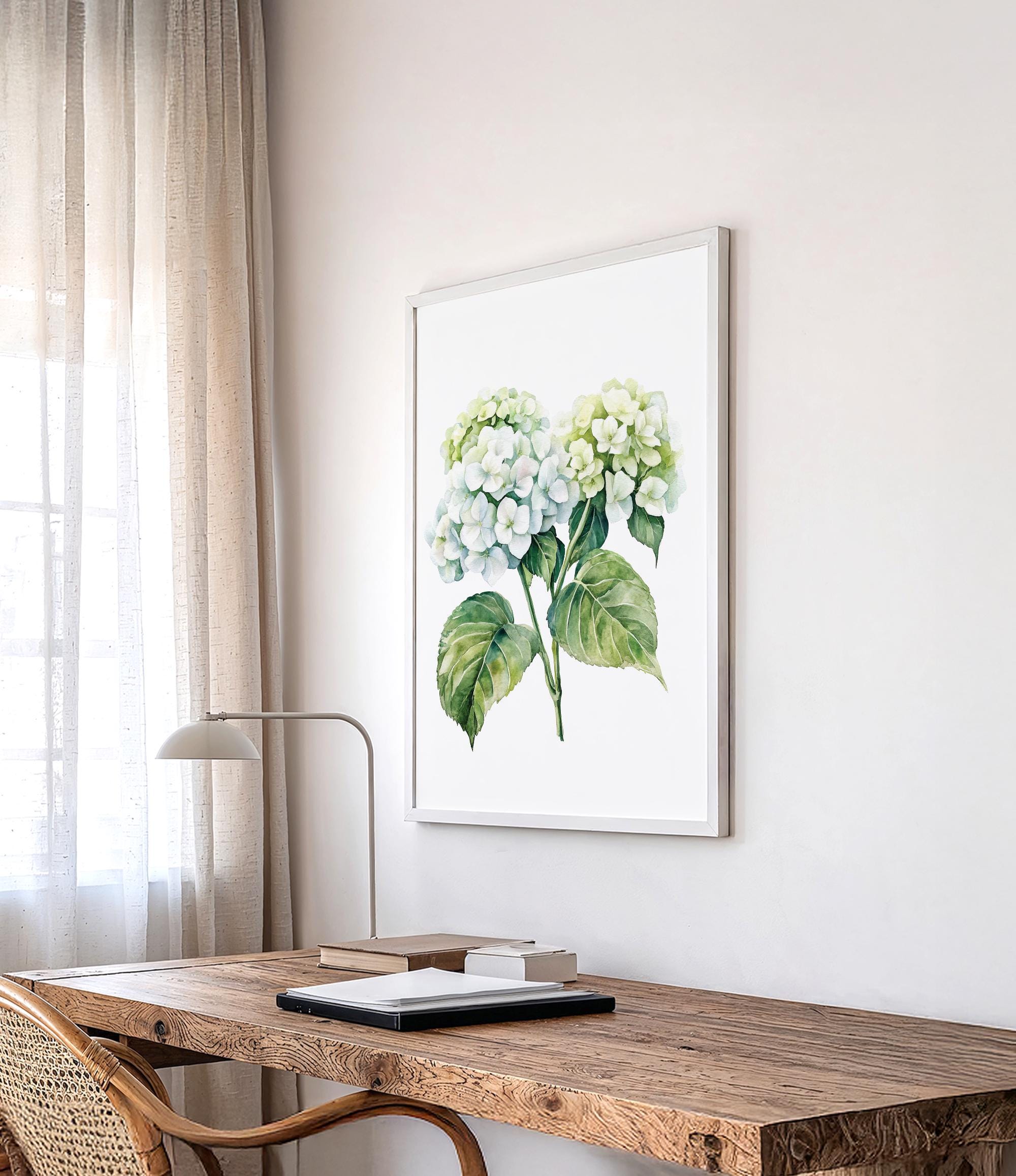a wooden desk with a lamp, a framed watercolor painting of green hydrangeas, and a window with sheer curtains.