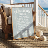 a beach house sign with a beach scene in the background, along with a wicker chair and some seashells on a wooden deck.