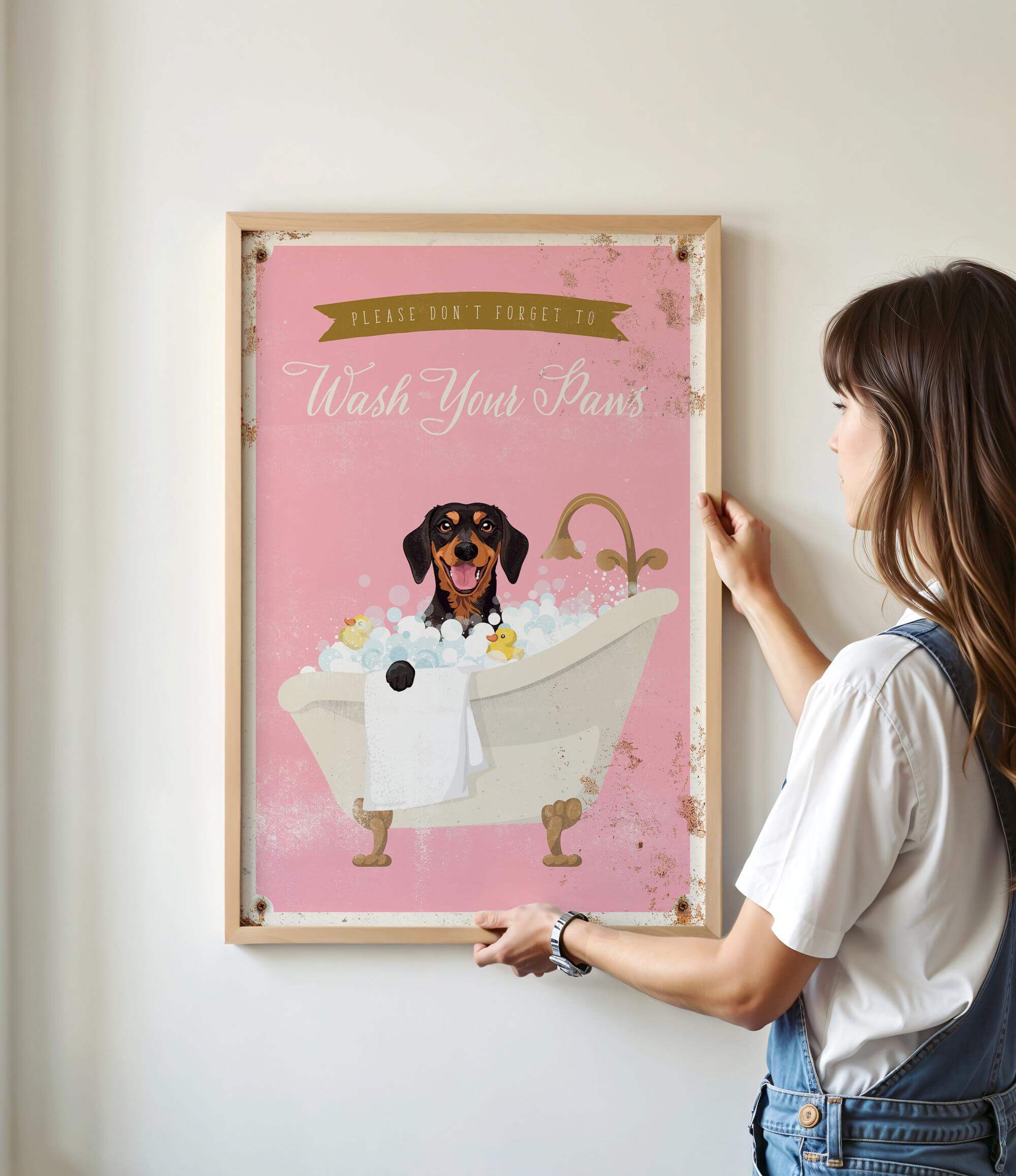 A woman is hanging a framed poster on a wall that features a dog sitting in a bathtub filled with bubbles.