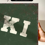 a hand holding a green canvas print with a white text or letter "K" on it.
