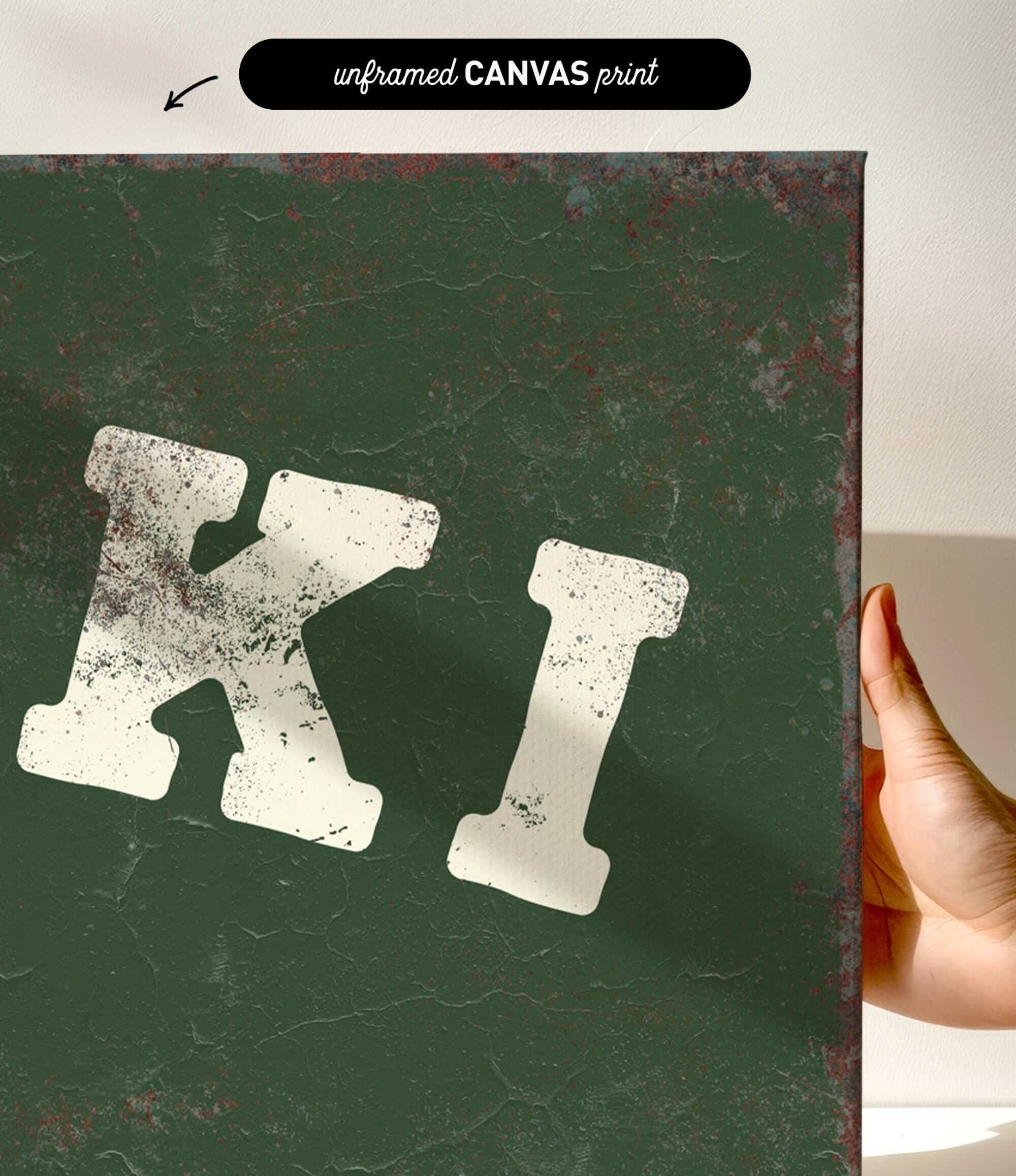 a hand holding a green canvas print with a white text or letter "K" on it.