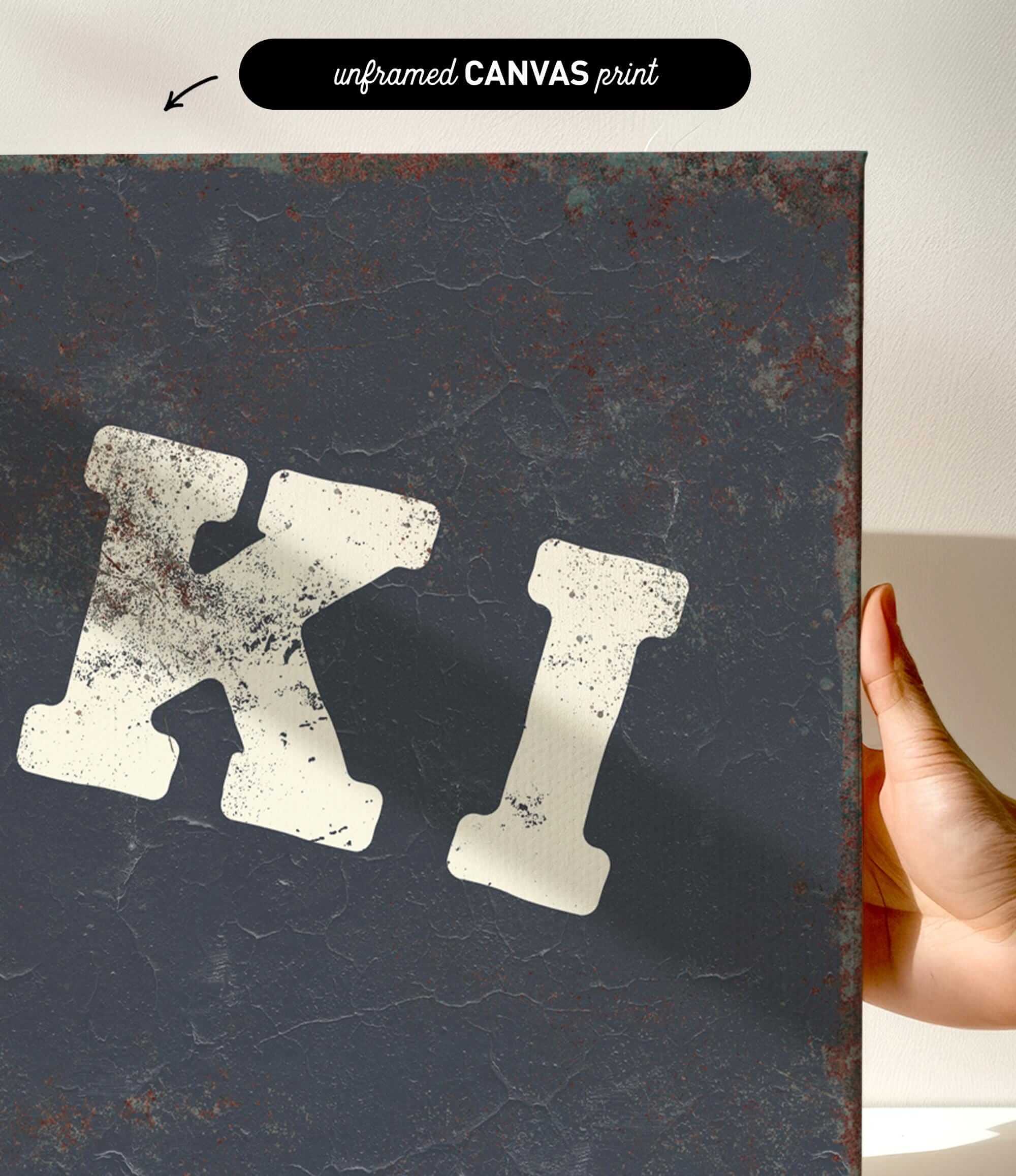 a hand holding a canvas print with a large, distressed letter "K" on it.