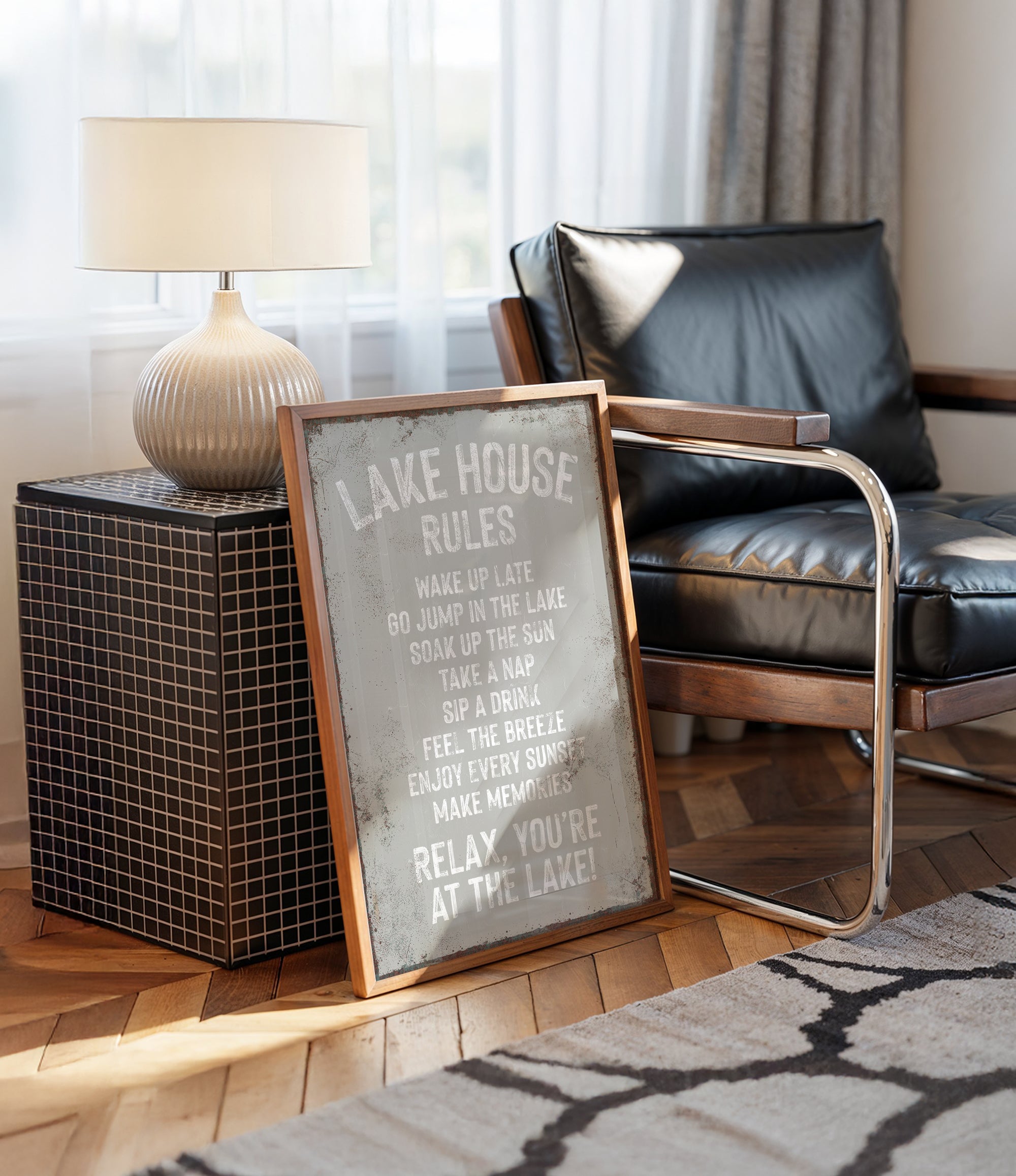a framed sign with a humorous message about lake rules, placed on a wooden floor next to a black leather chair and a lamp.