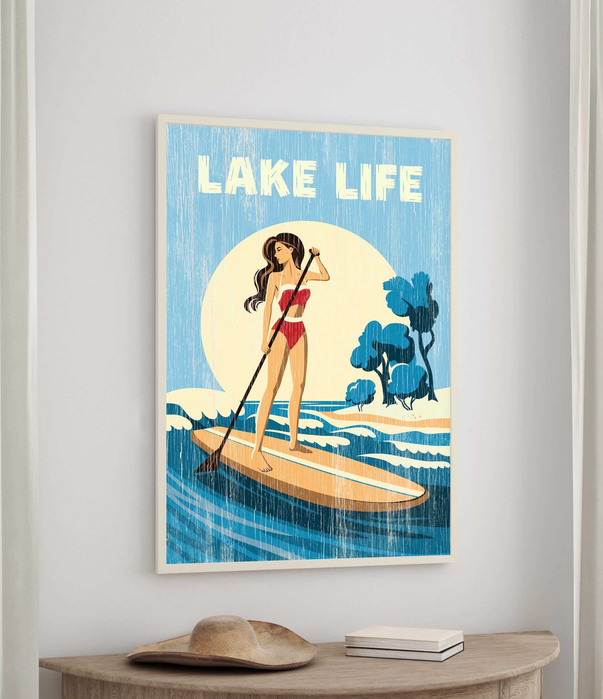 The image is a framed poster depicting a woman paddleboarding on a lake, with the text "LAKELIFE" prominently displayed.