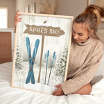 A woman sits on a bed holding the Cerulean Après Ski Signpost Wall Art—an ideal mountain lodge decor piece or vintage-inspired ski sign for your home.
