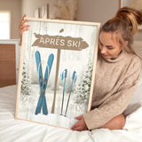 A woman sits on a bed holding the Cerulean Après Ski Signpost Wall Art—an ideal mountain lodge decor piece or vintage-inspired ski sign for your home.