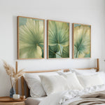 a bedroom with a bed, white pillows, and three framed prints of green leaves hanging on the wall above the bed.