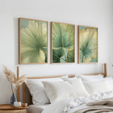 a bedroom with a bed, white pillows, and three framed prints of green leaves hanging on the wall above the bed.
