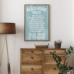A Beach House Rules Sign in painted wood (Tide) hangs above a wooden dresser with plants, bringing coastal wall art charm to this cozy room.
