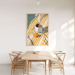 a dining room with a wooden table and four chairs, a bowl on the table, and a painting of a cup, lemon, and orange on the wall above the table.